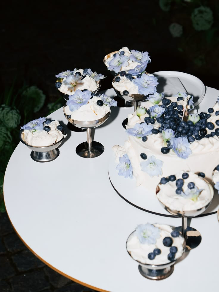 A wedding dessert table with a blueberry-topped cake and soft blue flowers